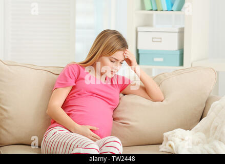 Schwangere Frau leidet unter Kopfschmerzen beim Sitzen auf dem Sofa zu Hause Stockfoto