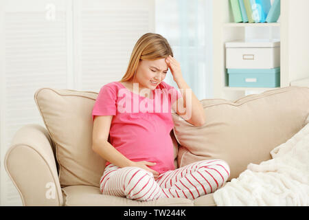 Schwangere Frau leidet unter Kopfschmerzen beim Sitzen auf dem Sofa zu Hause Stockfoto