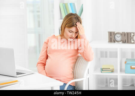 Schwangere Frau leidet unter Kopfschmerzen beim Sitzen am Arbeitsplatz im Büro Stockfoto