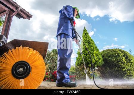 Männer tragen Industrielle nassen Mantel Reinigung Wohn- Auffahrt mit der Hochdruckreiniger. Stockfoto