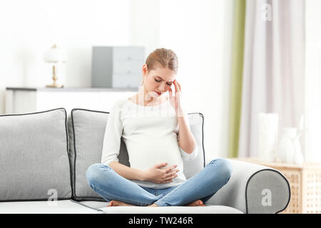 Schwangere Frau leidet unter Kopfschmerzen beim Sitzen auf dem Sofa zu Hause Stockfoto
