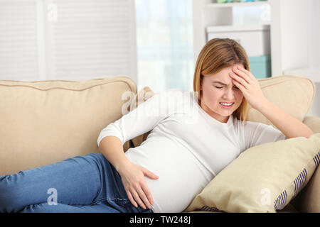 Schwangere Frau leidet unter Kopfschmerzen beim Liegen auf dem Sofa zu Hause Stockfoto