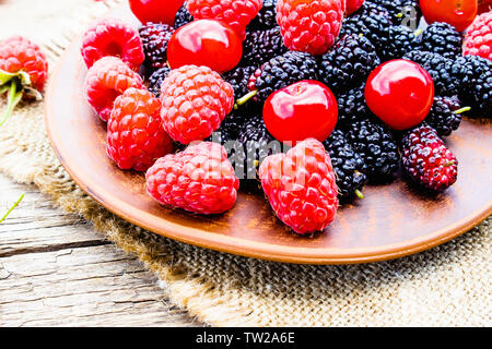Gemischte Beeren, Kirschen, Himbeeren, Maulbeeren in einer Schüssel auf der Leinwand und Holz- Hintergrund. Close-up Stockfoto