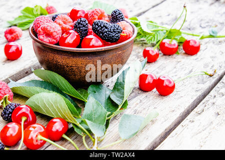Saftige frische und köstliche Beeren, Kirschen, Himbeeren, Maulbeeren in einer Schüssel auf Holz- Hintergrund. Close-up Stockfoto