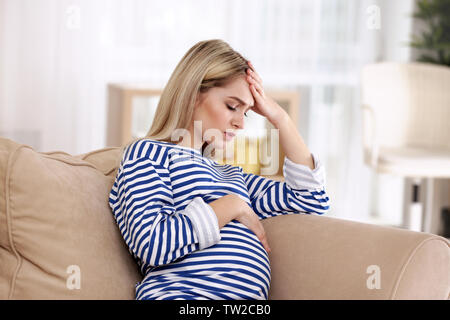 Junge schwangere Frau mit Kopfschmerzen zu Hause Stockfoto