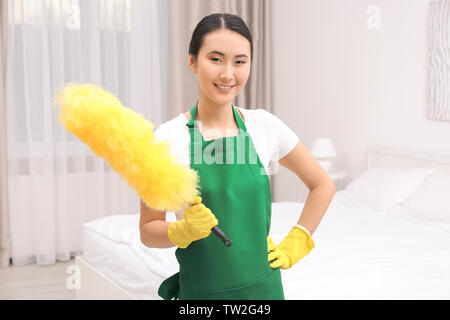 Junge weibliche Reiniger mit Duster bei der Arbeit im Schlafzimmer Stockfoto