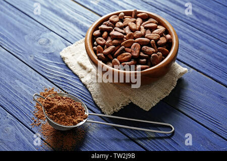 Kakaobohnen in der Schüssel und Sieb mit Puder auf hölzernen Tisch Stockfoto