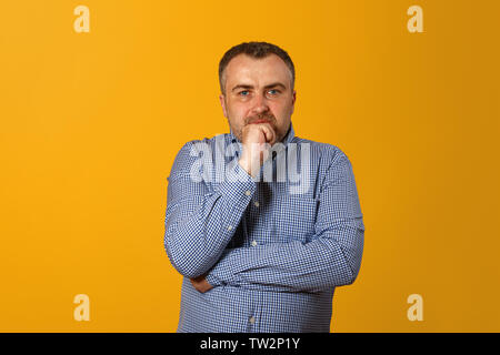 Nachdenklicher Mann mit der Hand am Kinn und Kamera. Gelber Hintergrund. Closeup Portrait. Stockfoto
