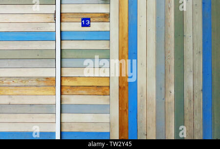 Haus Wand und Tür aus Holz bunt teilweise verblasst Bretter vertikal und horizontal angeordnet. Kleine blaue Schild mit der Nummer 13 auf Stockfoto