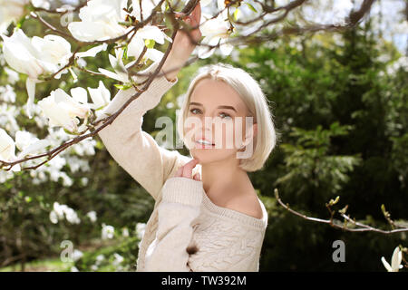 Junge blonde Mädchen in der Nähe von blühenden Magnolienbaum auf unscharfen Hintergrund Stockfoto