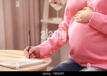 Schwangere Frau schreiben Babynamen in Notebook zu Hause Stockfoto