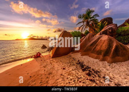 Eine identifizierte romantisches Paar am Ufer in der Nähe von geformten Granit Steine von Anse Source D'Argent mit coloful Sonnenuntergang Himmel. Seychellen, La Digue Flitterwochen Stockfoto