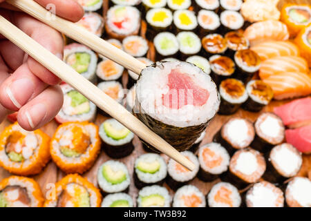 Fingern halten Stäbchen mit Thunfisch Nori über verschiedene Sushi und rollt auf hölzernen Tisch Rollen Stockfoto