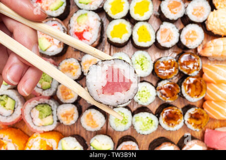 Blick von oben auf die Stäbchen mit Thunfisch Nori über viele Sushi und rollt auf hölzernen Tisch Rollen Stockfoto