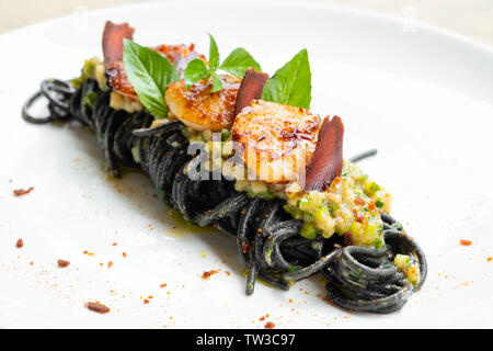 Der schwarze Tinte tagliolini Spaghetti mit Jakobsmuschel schließen, Erbsen Creme, Gemüse Zucchini frische Kräuter Basilikum, professionelle traditionellen italienischen Koch Isola Stockfoto