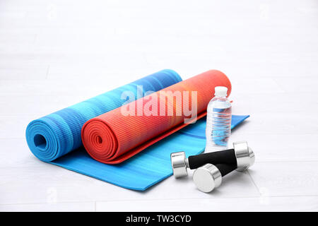 Zwei Yoga Matten mit Hanteln und eine Flasche Wasser auf Holzboden Stockfoto
