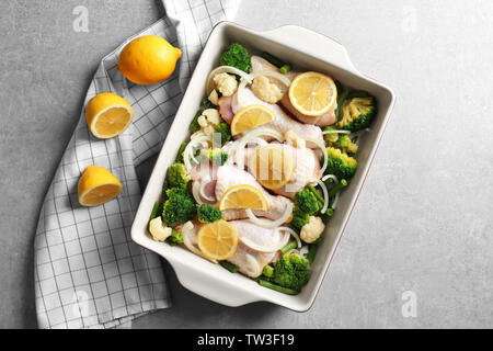 Raw Chicken Drumsticks mit Zitrone und Brokkoli in Auflaufform auf grau Tabelle Stockfoto