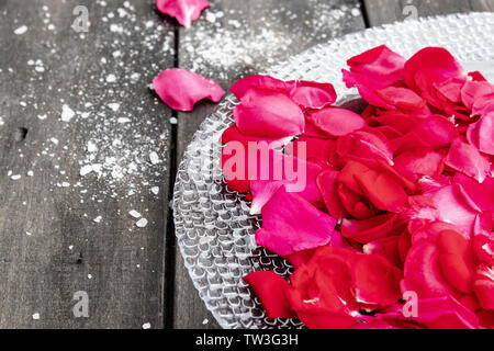 Rosenblätter liegen auf einer Platte auf alten, dunklen Holz. Stockfoto