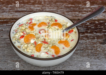 Frisches Frühstück mit Müsli, Joghurt, Nüsse, Goji Beeren, Chia Samen und Mandarin. Müsli mit Früchten und Beeren in der Schüssel auf einer hölzernen Hintergrund, in der Nähe Stockfoto