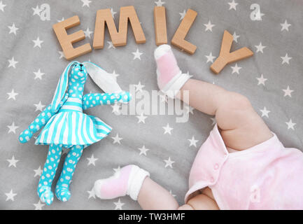 Beine von niedlichen Baby, Spielzeug und Wort EMILY aus Holz Buchstaben auf dem Bett. Auswahl name Konzept Stockfoto