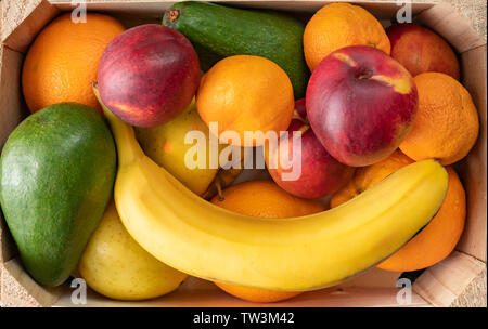 Große Holzkiste mit reifem Obst, Banane, Apfel, Orange, Mandarine, Avocado, vegetarische Essen Stockfoto