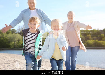 Glückliche Großeltern spielen mit kleinen Kindern am Flussufer Stockfoto