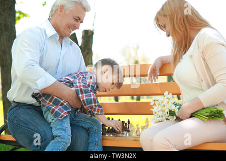 Süße kleine Jungen mit seinen Großeltern spielt Schach auf der Werkbank im Frühjahr Park Stockfoto