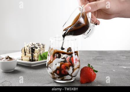 Weibliche Hand gießen Schokoladensauce auf Glas mit leckeren Dessert auf den Tisch Stockfoto