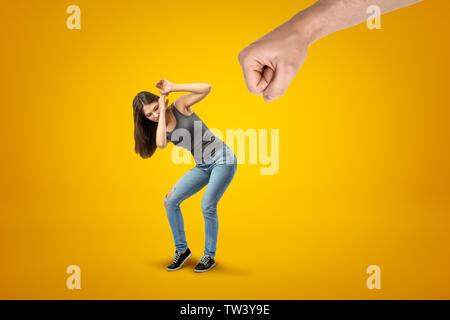 Junge brünette Mädchen mit lässigen Jeans und T-Shirt selbst Schutz von großen männlichen gedehnt Faust auf gelbem Hintergrund Stockfoto