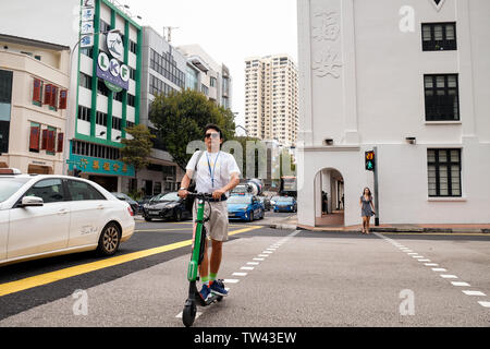 Ein alter Mann in Shorts, T-Shirt und Sonnenbrille verwendet einen elektronischen Roller eine Kreuzung in Singapur zu überqueren. Stockfoto
