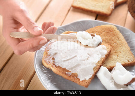 Weibliche Hand, die Löffel mit Kokosöl über leckeren Toast in der Platte Stockfoto