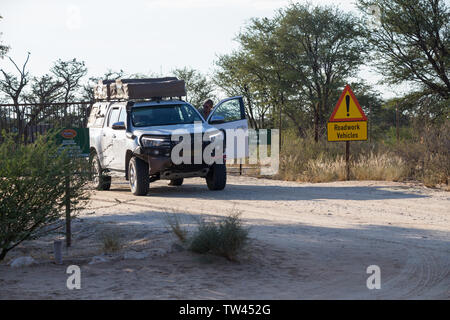 Weiß 4x4 off road Overland Camping Fahrzeug mit einem Mann in am Haupteingang nach Nossob Camp, Kgalagadi Transfrontier National Park Stockfoto