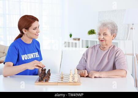 Junge weibliche Freiwillige schach spielen mit älteren Frau im Lichte Zimmer Stockfoto