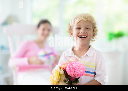 Happy Mother's Day. Kind mit Gegenwart und Blumen für Mama. Little boy Holding verpackte Geschenk und Blumenstrauß für die Mutter. Familie feiern Feder h Stockfoto