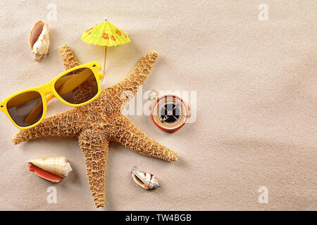 Komposition mit Seesternen, Sonnenbrille und Kompass auf Sand. Konzept für Reise und Urlaub Stockfoto