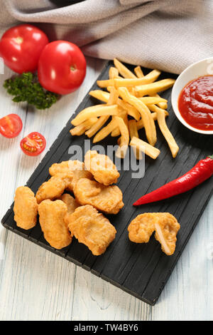 Lecker Nuggets, Pommes frites und eine kleine Schüssel mit Soße für Chicken auf Holzbrett Stockfoto