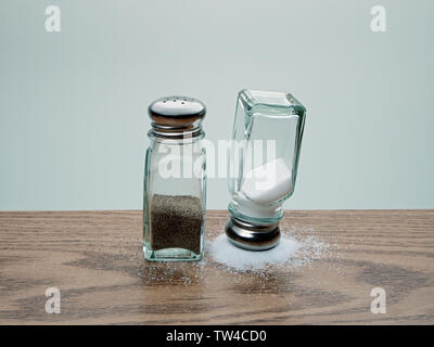 Balancing Trick mit der Oberseite nach unten Salt Shaker ausgeglichen durch verschüttetes Salz neben über Pfefferstreuer auf Holz Tisch gekippt Stockfoto