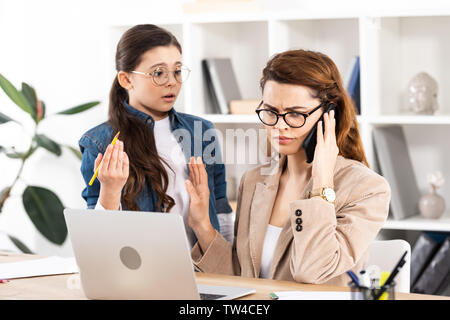 Kind mit Mutter sprechen auf Smartphone und Gestik im Büro überrascht Stockfoto