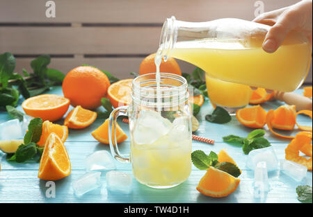 Junge Frau gießen Orangensaft aus Flasche in Glas Glas auf dem Tisch Stockfoto