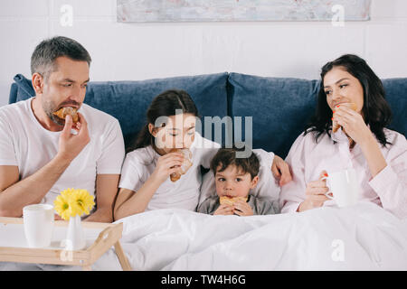 Glückliche Eltern und Kinder essen leckere Croissants im Bett Stockfoto