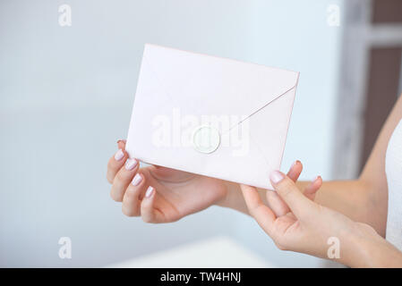 Nahaufnahme von weibliche Hände halten ein Silber Blau oder rosa Einladung Umschlag mit einem Wachs Dichtung, ein Geschenkgutschein, eine Postkarte, eine Hochzeit Einladung Stockfoto