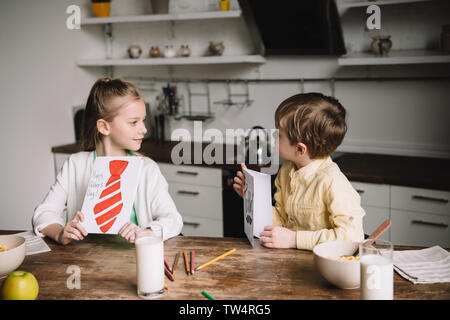 Adorable Kinder holding Vatertag Grußkarten während am Küchentisch sitzen mit Frühstück Stockfoto