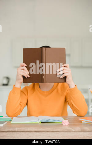 Schüler verstecken Gesicht hinter buchen Sie beim Sitzen am Schreibtisch und Hausaufgaben Stockfoto