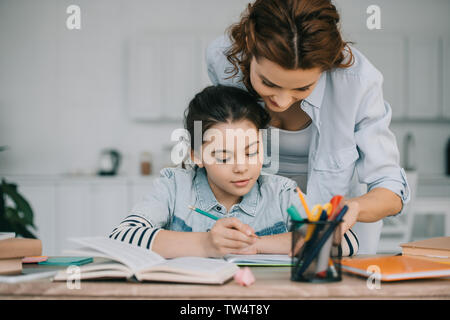 Adorable Kind schreiben in Kopie buchen Sie bei Schularbeiten in der Nähe von Mutter Stockfoto