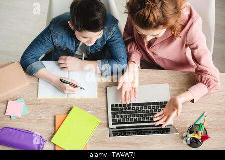 Blick von oben auf die Mutter und der Sohn sitzt am Schreibtisch mit Laptop und Notebooks und zusammen Hausaufgaben Stockfoto