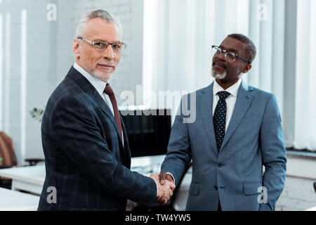 Selektiver Fokus der glücklichen Geschäftsmann in Gläser Händeschütteln mit afrikanischen amerikanischen Partner Stockfoto