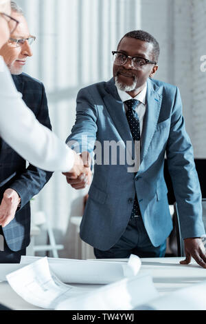 Selektiver Fokus der Geschäftsmann in Gläsern an afrikanischen amerikanischen Mann Händeschütteln mit Frau im Amt suchen Stockfoto