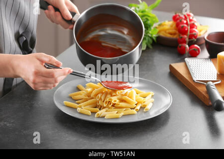 Frau hinzufügen lecker Tomaten Soße zu Nudeln auf dem Teller Stockfoto