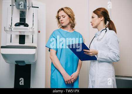 Radiologen mit Zwischenablage, umgekippt, Frau beim Stehen in der Nähe von x-ray Maschine Stockfoto