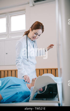 Selektiver Fokus der hübschen Lächeln Radiologe Vorbereitung des Patienten für die Untersuchung im MRT-Gerät Stockfoto